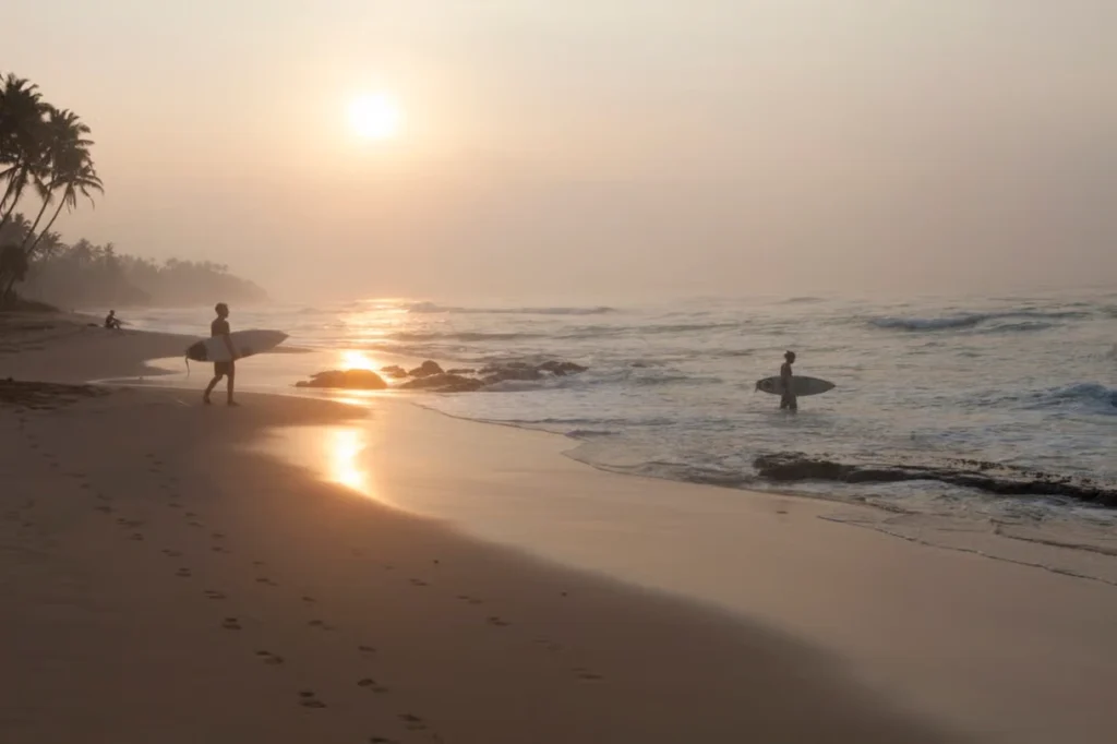 Surfers walking along Arugam Bay Beach during golden hour on Sri Lanka’s east coast.