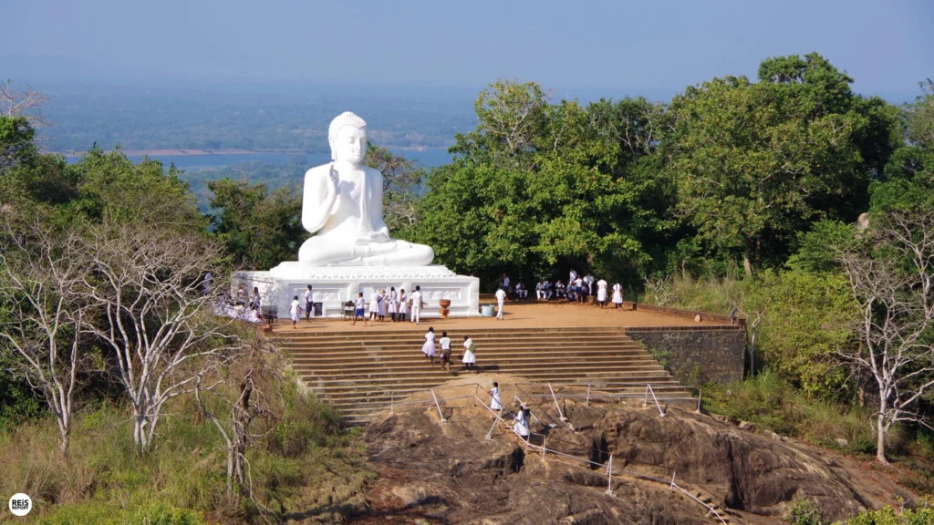 Large white Buddha statue overlooking the forested landscape from Mihintale near Anuradhapura, Sri Lanka.