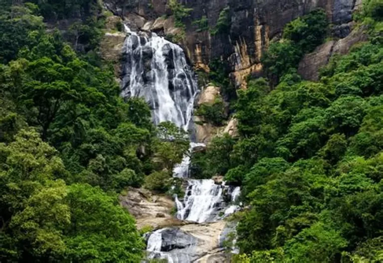 Ravana Falls cascading over a rocky mountainside surrounded by lush tropical forest near Ella, Sri Lanka.