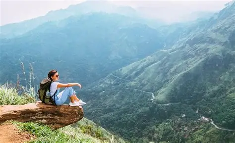Solo female traveller sitting at a scenic viewpoint overlooking dramatic green mountains and valleys in Sri Lanka.